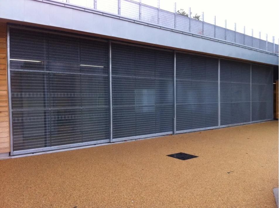 Run of galvanised sliding mesh security screens across the glazed elevation of a Sheffield youth centre